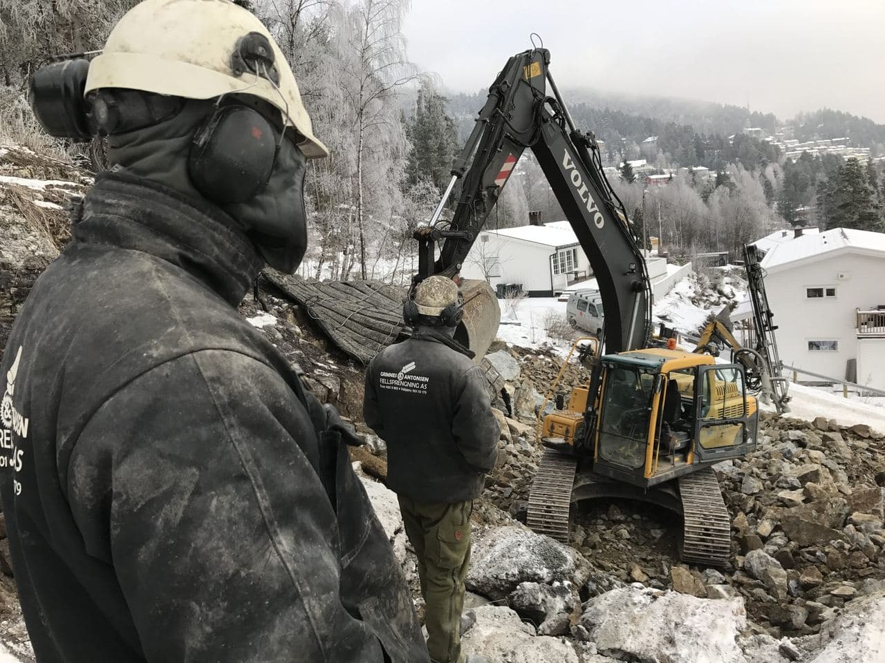 En av oss med hørselvern følger med mens gravemaskinen jobber på en tomt i et boligfelt om vinteren.