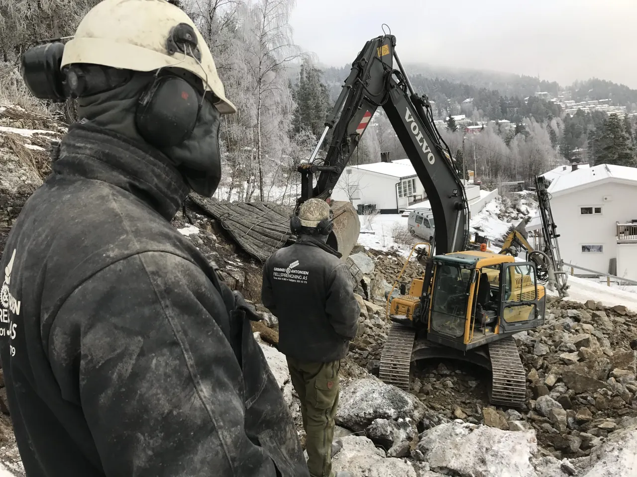 En av oss med hørselvern følger med mens gravemaskinen jobber på en tomt i et boligfelt om vinteren.